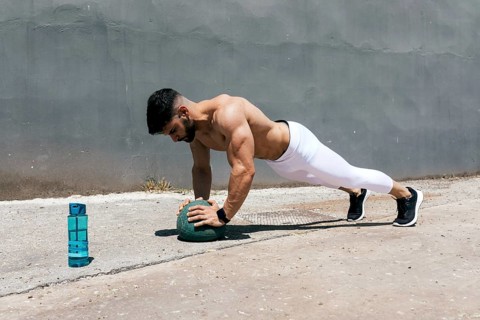 Athletic man outdoors performing a plank exercise using a medicine ball. He is showcasing strength
