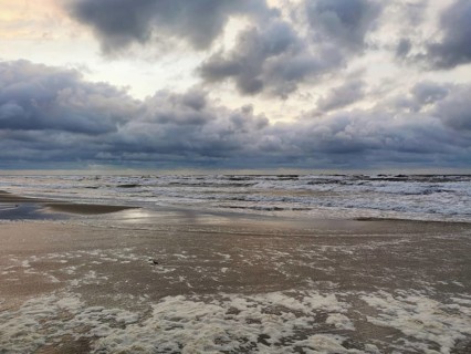 Dramatic sky over the sea at dusk with clouds and waves, foam along the coastline
