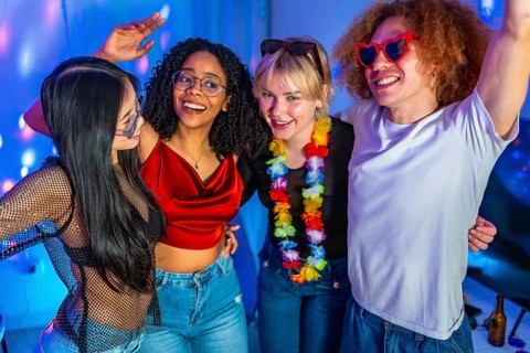 Four cheerful multi ethnic friends are dancing and having fun at a party with blue disco lights