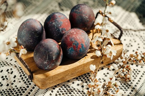 Artistic galaxy-themed Easter eggs displayed on a wooden tray, surrounded by spring blossoms on a