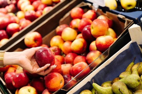 A hand holds a red apple above a display filled with assorted apples and pears. The scene