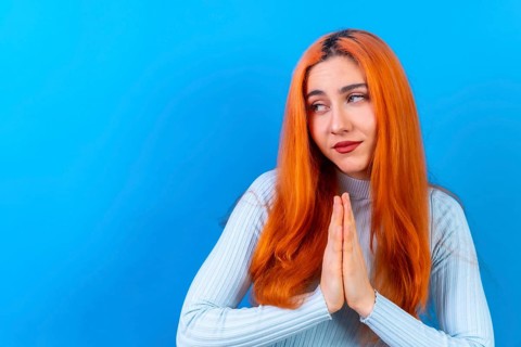 Redhead woman in studio photography making the gesture please on a blue background