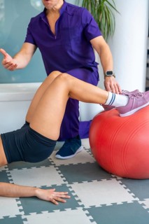 Physiotherapist guiding a woman performing physical therapy exercises using a fitness ball for