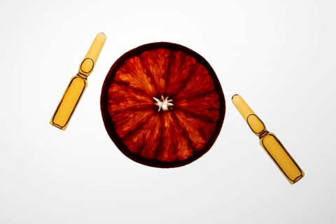A sliced orange and two ampoules create a vibrant health and wellness theme on a white background.