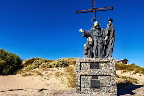 Monument statue with monks and cross in a dune landscape under bright blue sky, monument by