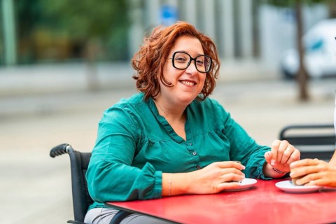 Woman with disability using electric wheelchair drinking coffee with friend sitting in an outdoor