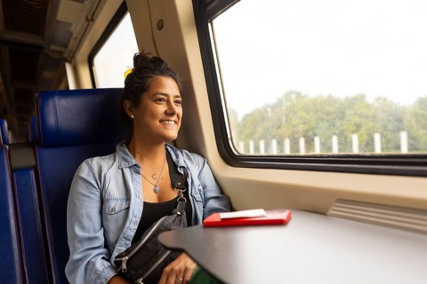 A cheerful woman enjoys a scenic train ride, gazing out the window at lush green landscapes A red