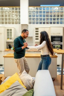 Young multi ethnic couple smiling and holding hands while dancing in a modern open plan kitchen and