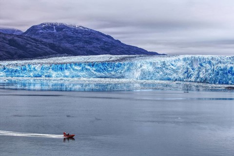 A small boat sails along the impressive Bruges Glacier, which stretches along the edge of the