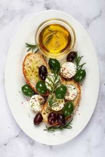A plate with a snack, ciabatta bread with cheese and olives, olive oil, spices and herbs, top view,