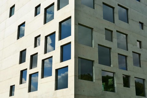 A modern building with numerous square windows in front of a blue sky with clouds, School of