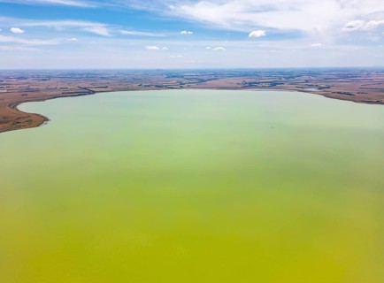 Aerial photograph capturing a vast, calm green lake surrounded by expansive, flat countryside in