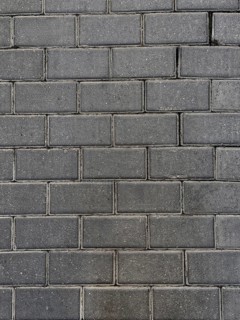A close-up view of a dark stone brick wall, showcasing its rough texture and the pattern formed by