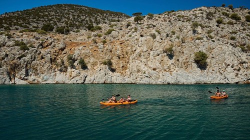 People enjoy paddling in kayaks along the rocky coast on the clear sea, Rina, harbour, Vathi,