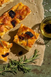 Freshly baked homemade focaccia slices garnished with rosemary and sun dried tomatoes on parchment