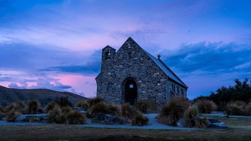 The small church The Church of the Good Shepherd on Lake Tekapo with a cloudy sky at sunset.