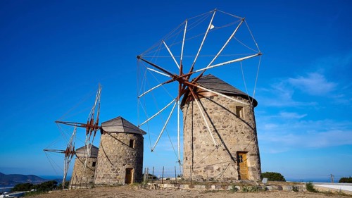 Two fragmented stone windmills under a clear blue sky in a natural setting, windmills, on a ridge,