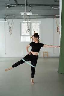 A woman in athletic wear performs a yoga exercise using a resistance band in a studio. The setting
