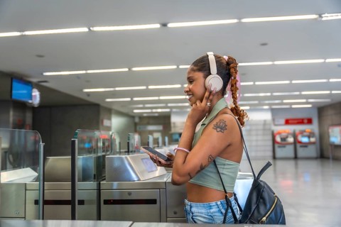 Young black woman listening to music with headphones and smartphone, smiling while passing through