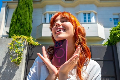 Redhead woman smiling with closed eyes, holding a smartphone in a magenta case featuring a magnetic