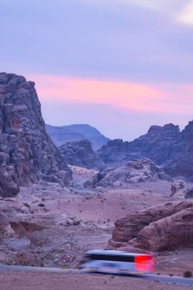 White passenger coach bus driving asphalt road winding through sandstone rock mountains canyon