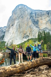 Five friends stand on a fallen log by the merced river, cheering and waving with el capitans