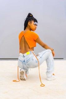 A young trap dancer with braids. Black ethnic girl with orange t-shirt and cowboy pants. Backs of