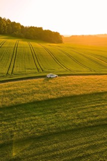 A car drives alone through the fields under a golden evening sky at sunset, Tesla Model Y,