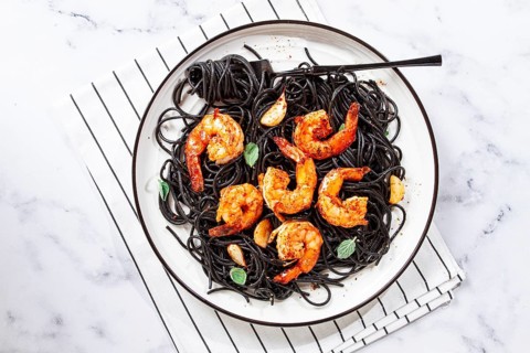 Black spaghetti with shrimp, on a white plate with a fork, on a striped napkin, marble background,
