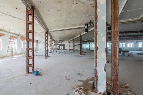 A large space under renovation, showcasing exposed steel beams and construction equipment. Natural