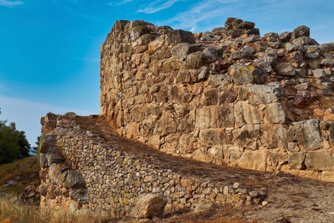 Cyclopean wall, old stone ruins under blue sky, with natural surroundings and historical flair,