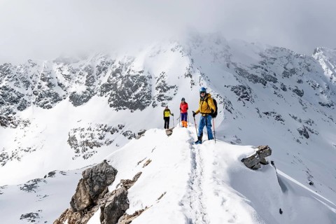 Three mountaineers climbing up the narrow mountain ridge of Piz Laviner, view of wintry mountain