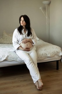 A serene pregnant woman sits on a bed, cradling her belly, symbolizing the beauty and anticipation