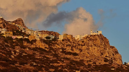 A village on a rocky cliff in the warm morning light with impressive clouds, mountain village