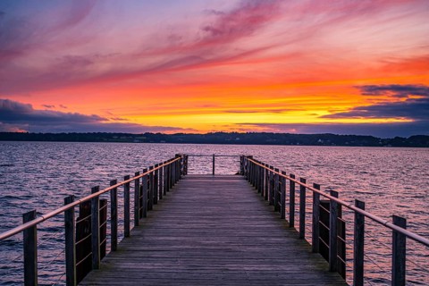 Wooden jetty juts into the sea during a spectacular sunset with intense colours in the sky,