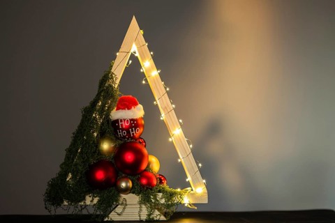 Modern DIY wooden Christmas tree with LED lights, moss, red balls and ornaments on a neutral