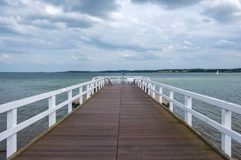 A wooden jetty stretches into a lake under a cloudy sky, Hohwacht, Schleswig-Holstein, Germany