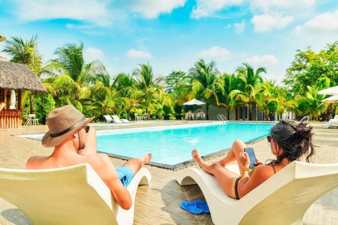 Couple lay on sunbeds enjoy sunbathing relax scroll phone internet on all-inclusive vacation
