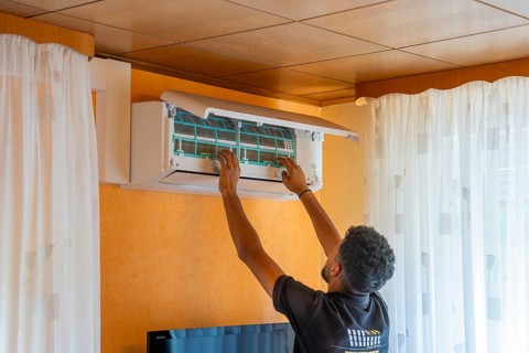 A man installs an air conditioner in the living room with white curtains, air-conditioning and