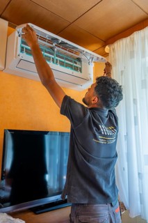 A man installs an air conditioner in the living room next to a television, air conditioning and