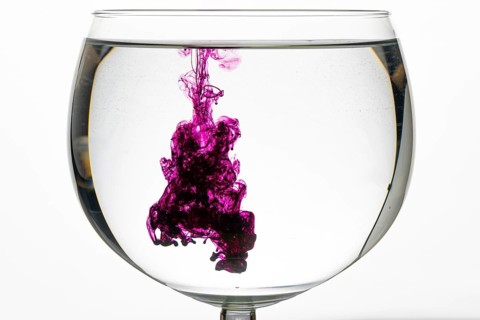 Violet ink mixes artistically in the clear water of a glass