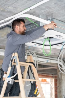 Professional hvac technician on ladder installing ceiling air conditioning unit, piping and