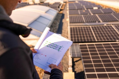 A person looks at construction plans in front of solar modules on a roof, PV installation at OBI