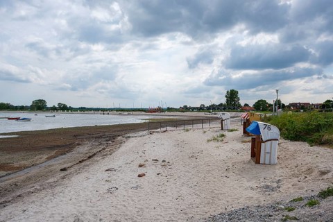 A quiet stretch of beach with beach chairs and boats under a cloudy sky, Hohwacht,