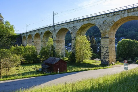 Large stone viaduct with several arches over a green landscape, bright sky and a small road,