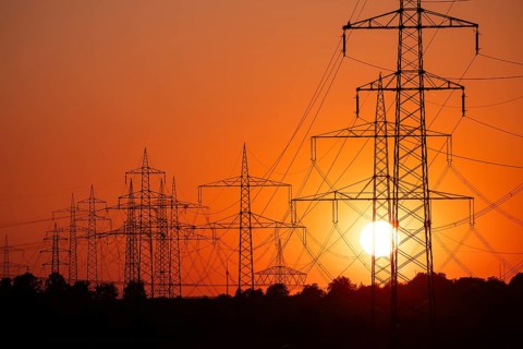 Silhouette of several high-voltage power lines and electricity pylons against a glowing orange and