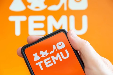 Hand holding mobile phone with Temu logo online marketplace online commerce ecommerce on computer