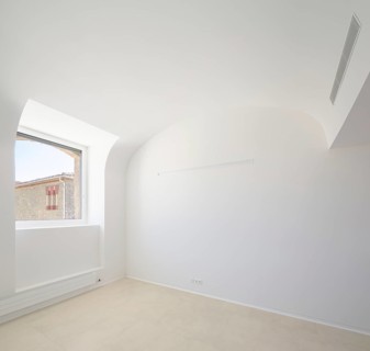 A spacious empty room of hospital with clean white walls, a large window providing natural light,