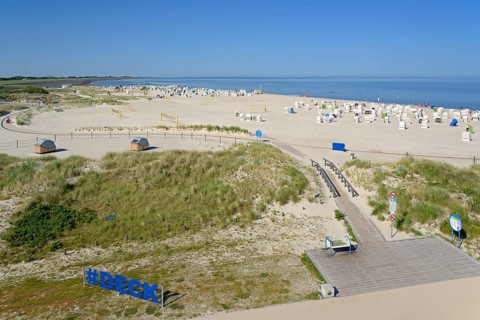 View over the dune landscape to the beach with beach chairs and areas for sports, blue sky, North