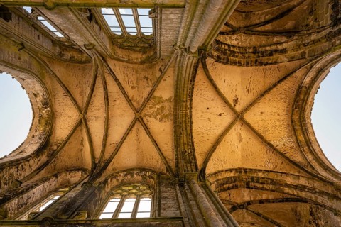 Looking up into the stone cross-rib vault of a Gothic church ruin looking at the sky through the
